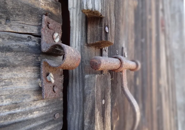 Chiusura arrugginita su una porta di legno usurata, simbolo di una backdoor: accesso secondario e invisibile all’interno di sistemi apparentemente sicuri
