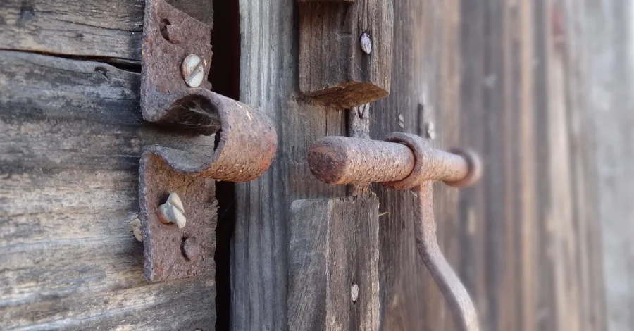 Chiusura arrugginita su una porta di legno usurata, simbolo di una backdoor: accesso secondario e invisibile all’interno di sistemi apparentemente sicuri